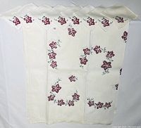 Full view of vintage white tablecloth and eight matching napkins showing embroidered red floral designs with green stems.