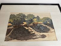 Close view of the framed painting showing the Vietnamese village scene with trees, houses, and shadows cast on the ground. Signed in lower right.