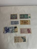 Seven international paper banknotes from different countries laid out on a light surface to show front designs and condition.