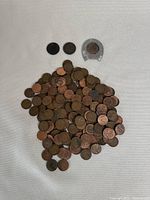 Image of a large pile of various Canadian and American pennies in circulated condition with a large silver coin case containing a penny.