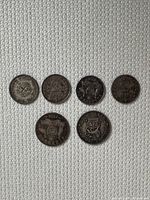 Top view of seven British silver pence coins arranged on fabric, showing front and back sides of various coins including date and denomination symbols.