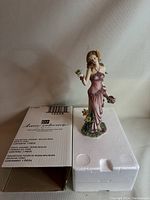 Full view of the figurine standing on its original white styrofoam insert alongside its cardboard box, showing overall size and packaging.