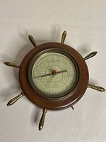 Full view of circular Taylor Instruments barometer housed in wooden ship wheel frame with brass handles.