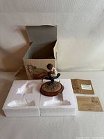 Photo showing figurine on styrofoam packaging with open original box and papers behind