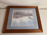 Framed winter landscape print by Tom Thomson with wooden frame and blue matting.