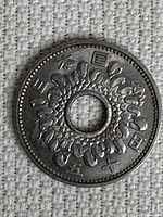 Obverse side of the vintage Japanese 50 yen coin showing Japanese characters and a wreath design around a circular hole in the center.