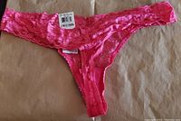 Pink lace thong panty laid flat showing front side with I.N.C. size and brand tags visible, color vibrant pink, lace floral pattern.
