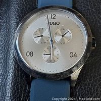 Close-up photo of the watch face showing the silver dial with three subdials and blue silicone strap.