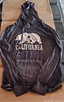 Front view of dark grey women's pullover hoodie with white California bear logo and text, hood with drawstrings visible, laid flat.