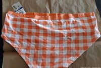 Photo of front side of orange and white gingham checkered bikini style underwear with elastic waistband.