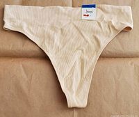 Front view of the seamless ribbed thong in chai color showing the smooth, seamless finish with ribbed texture and tag attached.