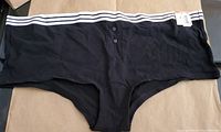 Photos show front and back views of a solid classic black women's underwear by Jenni X with a white striped waistband and front button detail, new with tags attached.
