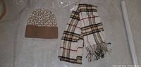Photo showing the Michael Kors hat with MK logo pattern next to the plaid scarf to illustrate both items in the lot.