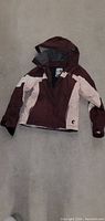 Full view of the maroon and light pink Roxy jacket with hood, laid flat on floor.