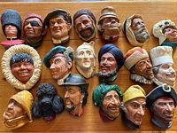 Photo showing 19 Bosson ceramic heads with various characters and costumes arranged in rows on a wooden surface.