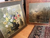 Two framed paintings placed side by side, showing a floral still life and a landscape scene.