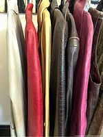 Side view of six leather jackets hanging on a rack showing different colors and textures including beige, red, yellow, brown crocodile pattern, purple, and brown leather.