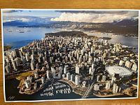 Aerial photographic print of downtown Vancouver with marina, stadium, and mountains in background, signed by photographer.