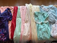 Grouped view of the 12 pieces of vintage lingerie including nighties, bathing suit, bed jackets, pyjama set, and robe in various pastel shades.