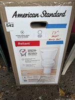 Photo of sealed box with American Standard label, showing model Reliant, round front bowl, white color, 17" chair height, missing seat indicated on tape.