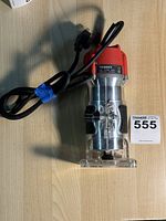 Full view of electric router trimmer showing metal body, red plastic housing, power cord, and transparent base.