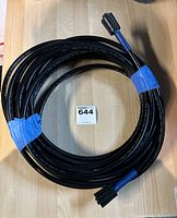 Coiled black pressure washer replacement hose with blue end caps on wooden surface