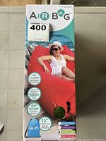 Front of original box showing red air chair with woman lounging on it. Labels note no pumps needed, holds 500+ lbs, rip stop material, 15" carrying bag, multiple colors available.