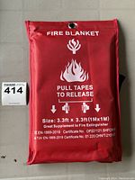 Photo of the fire blanket pouch with printed instructions and certifications visible, showing size and release instructions.