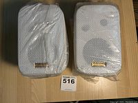 Pair of white Pyramid outdoor/marine speakers in plastic wrapping with mounting brackets and labels visible