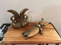Photo of two brass swan bookends and one brass boot scraper on a wooden surface
