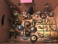 Overall view of the lot showing various brass animals, bells, and the tic tac toe game in a cardboard box