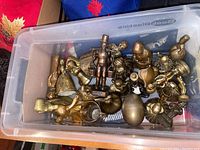 Plastic bin containing a collection of small brass figurines and decorative pieces of varying shapes and sizes