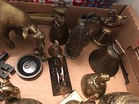 Overhead view of large brass bull, small brass figurines including a woman with a hat, and various brass decorative objects and bells.