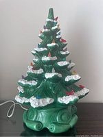 Front view of vintage green ceramic Christmas tree with white snow accents and colorful plastic lights on branches. Electrical cord attached.