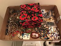 Lot contents showing assortment of costume jewelry and floral decorative box with lid on