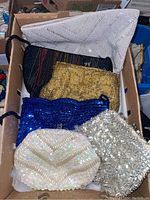 Photo showing six women's evening bags in a box with various colors and beaded/sequined designs.