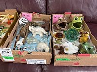Two cardboard boxes containing assorted bear and frog figurines made from ceramic, glass, wood and metal.