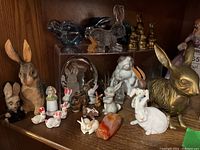 Wide view of all rabbit figurines on wooden shelf displaying assortment of materials and colors.