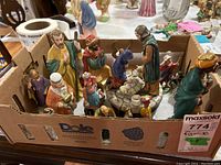 Wide shot of the entire nativity figurine set and wise men in a cardboard box, showing multiple figurines arranged closely together with detailed coloring and materials.
