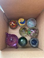 Top view of eight glass paperweights and one green glass insulator in a cardboard box