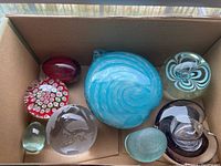 Photo showing seven paperweights of various designs including swirled, spherical, millefiori, and textured glass styles.
