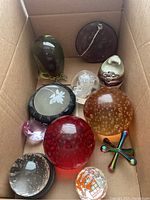 Wide shot of a box with various glass paperweights and the metallic jack showing shapes, colors, and textures