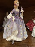 Side view of Royal Doulton porcelain figurine 'Nicola' showing the lady in purple floral dress holding a bird.