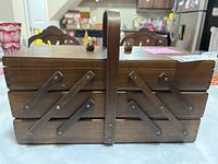 Closed wood expandable sewing box with a handle and two knobs on top on a table.