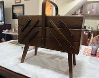 Side view of closed wood expanding sewing box with handle and angled legs on a table.