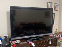 Front view of Sony Bravia 52-inch TV on wooden console with remote control on the base stand.