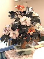 Front view of stone tree with black leaves, pastel rock flowers, and textured trunk in green stone base.
