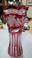Full view of the cranberry and clear glass vase showing floral cut patterns and scalloped rim.