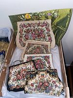 Top-down image showing all five tapestry evening bags with floral needlepoint and embroidery in a box.