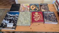 Full view of eight hardcover books on a wooden table showing book covers and general condition of the lot.